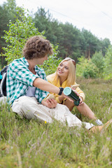 Male hiker pouring coffee for woman while relaxing in field