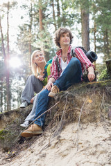 Naklejka na ściany i meble Full length of hiking couple sitting on edge of cliff in forest