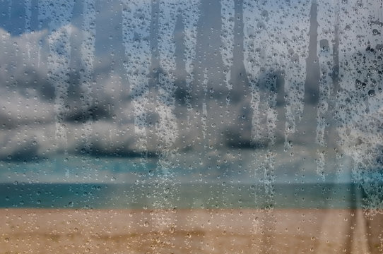 View through glass window with water drop to raining weather on the beach