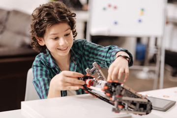 Amused teen boy programming digital robot in the studio
