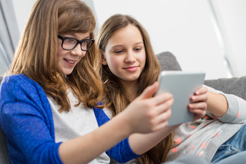 Sisters using digital tablet together at home