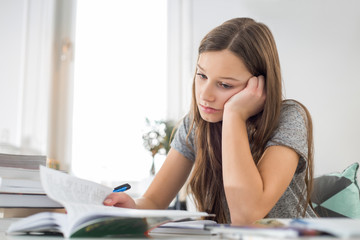 Bored girl studying at table in house