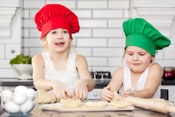 Two cheerful girls cook in colored caps prepare dough