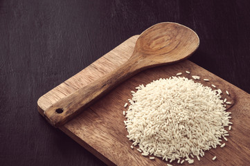 Heap of raw jasmine rice with wooden spoon on table
