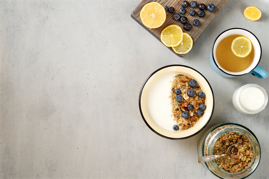A healthy breakfast with yogurt and granola, tea with lemon. Gray wooden background, top view