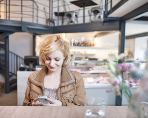 Happy young woman reading text message on cell phone in cafe