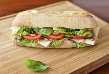 Delicious ciabatta sandwich with ham, tomatoes, fresh salad and cucumber slices.