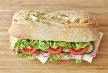 Delicious ciabatta sandwich with ham, tomatoes, fresh salad and cucumber slices.