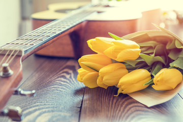 Beautiful spring background music. Guitar, yellow tulips, musical page on a dark wooden background. Shallow depth of field. Coloring and processing photo with soft focus in instagram style. - obrazy, fototapety, plakaty