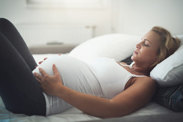 Beautiful pregnant woman lying in bed with cramps
