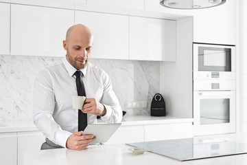 Mid adult businessman having coffee while using tablet PC at kitchen counter