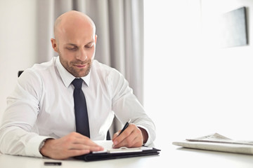 Mid adult businessman writing on clipboard in home office