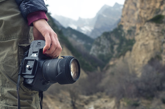 A female hand holds a camera against a mountain landscape