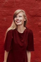Naklejka premium Stunning blond in red dress against red wall, smiling