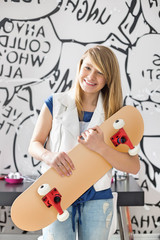 Fototapeta premium Portrait of happy teenage girl holding skateboard at home