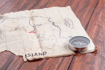 Treasure Map of fake Island with compass and red cross on wooden table background. Adventure concept