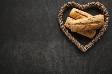 Concept of gluten free buns for allergic people with disease. Variation of bread with wooden heart shape on dark background.