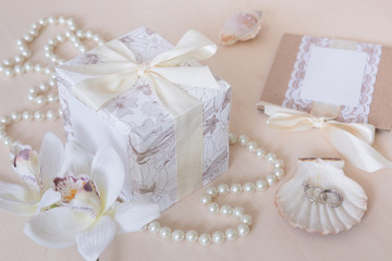 Present, beads, seashells, orchid and rings on wooden background