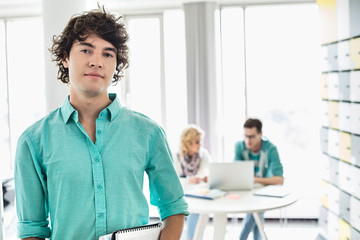 Fototapeta premium Portrait of confident businessman with colleagues working in background at creative office
