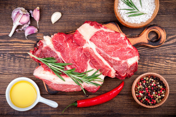Meat with herbs and spices on wooden background. Raw beef steak on cutting board with rosemary and garlic. Ingredients for cooking meat. Top view, copy space