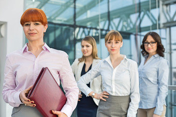 Portrait of confident businesswoman holding folder with female colleagues standing in background