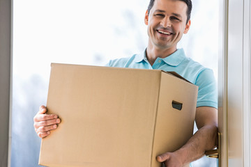 Happy man carrying cardboard box at entrance of new house