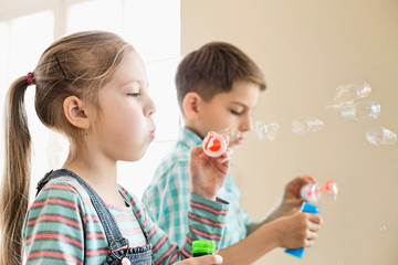 Brother and sister playing with bubble wands at home