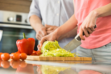 Midsection of woman chopping vegetables in kitchen with man standing in background
