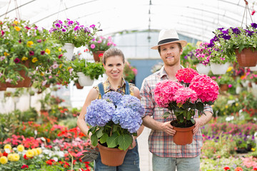 Portrait of smiling gardeners holding flower pots at greenhouse