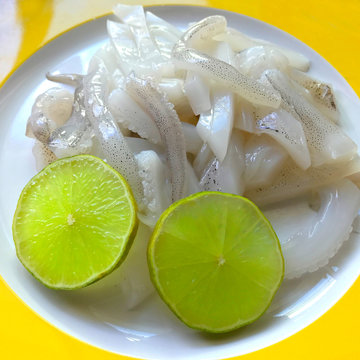 Fresh uncooked sliced squid on yellow dish with two slice of lime