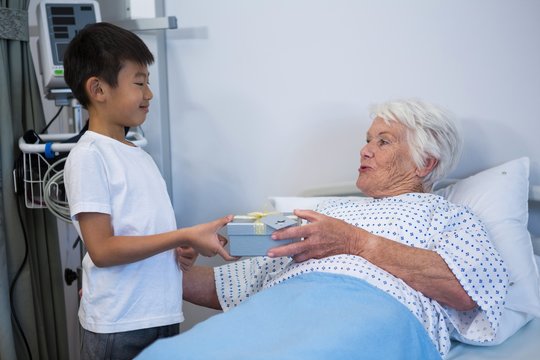 Boy giving a gift to senior patient on bed