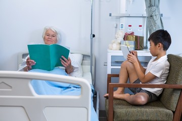 Senior patient reading a book while boy using digital tablet