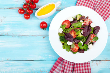 Fresh salad with spinach, arugula, broccoli, tomato, mozzarella cheese, chard leaves and olive oil on wooden background. Healthy food and diet concept. Vegetarian food. Copy space. Top view