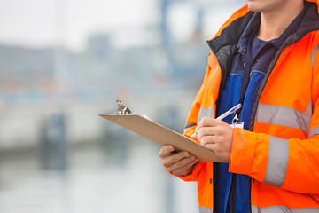 Midsection of mid adult man writing on clipboard in shipping yard - Powered by Adobe
