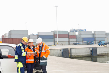 Workers using tablet PC beside car in shipping yard