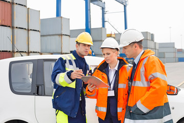 Workers discussing over clipboard beside car in shipping yard