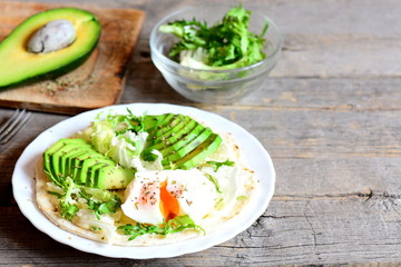 Healthy egg breakfast. Poached egg, avocado slices, cabbage, lettuce mix, tortilla, sauce and spices. Egg and avocado tortilla on plate and on vintage wooden background with copy space for text