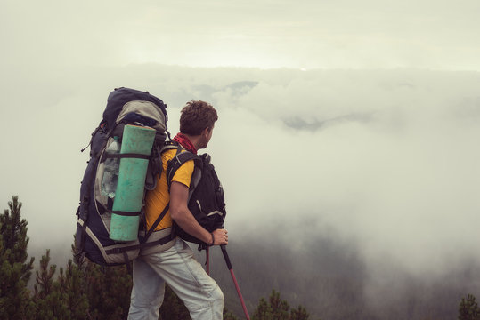 Man with big backpack stands in the mountains over the clouds