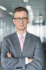 Fototapeta premium Portrait of middle-aged businessman standing with arms crossed in office