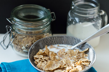 Breakfast cereal with crispy flakes, granola, nuts and oats with milk in a small grey bowl with metal spoon