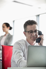 Businessman talking on telephone with colleague in background at office