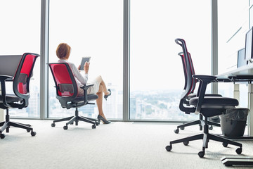 Full length of young businesswoman using tablet PC on chair in office