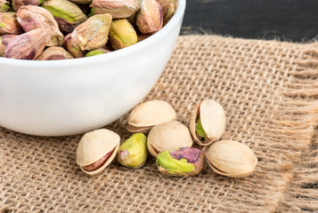 Pistachios unshelled in a bowl with scattered nuts on burlap