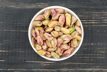 Pistachio nuts without shell in a bowl on a wooden background, top view