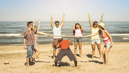 Multiracial happy friends group having fun together with limbo game at beach - Summer joy and friendship concept with young multi ethnic people playing on spring break vacation - Retro vintage filter - obrazy, fototapety, plakaty
