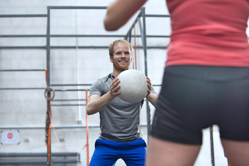 Fototapeta na wymiar Happy man throwing medicine ball towards woman in crossfit gym