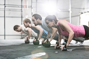 Fototapeta na wymiar Side view of determined people doing pushups with kettlebells at crossfit gym
