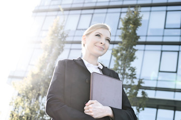 Low angle view of thoughtful businesswoman holding folder on sunny day