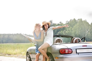 Naklejka premium Woman showing something to friend with map while leaning on convertible