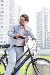 Businessman answering mobile phone while standing with bicycle outdoors